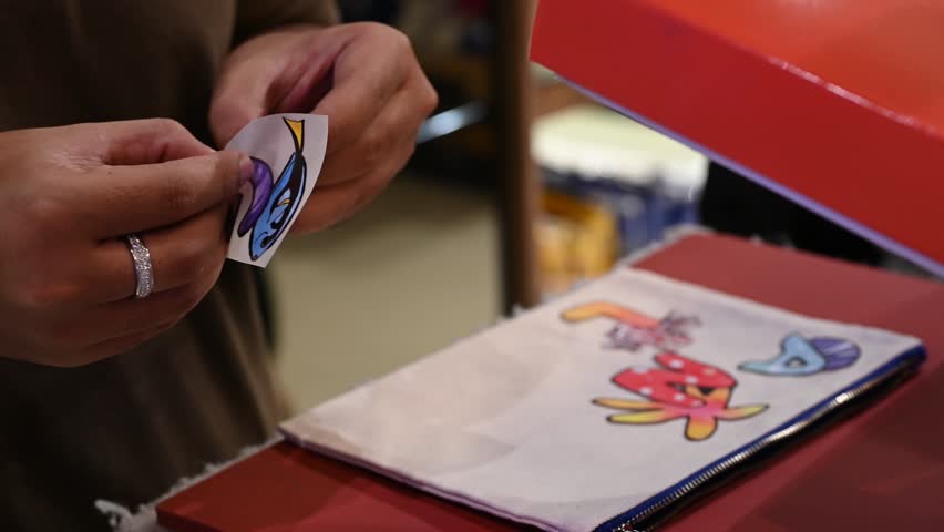 Bangkok, Thailand - 18th December 2025: Man manually printing alphabets on a pouch using an industrial printing machine, showcasing hands-on packaging, craftsmanship, manufacturing process, and small-scale production.