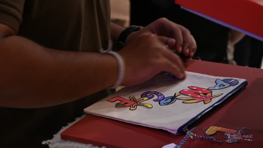Bangkok, Thailand - 18th December 2025: Man manually printing alphabets on a pouch using an industrial printing machine, showcasing hands-on packaging, craftsmanship, manufacturing process, and small-scale production.
