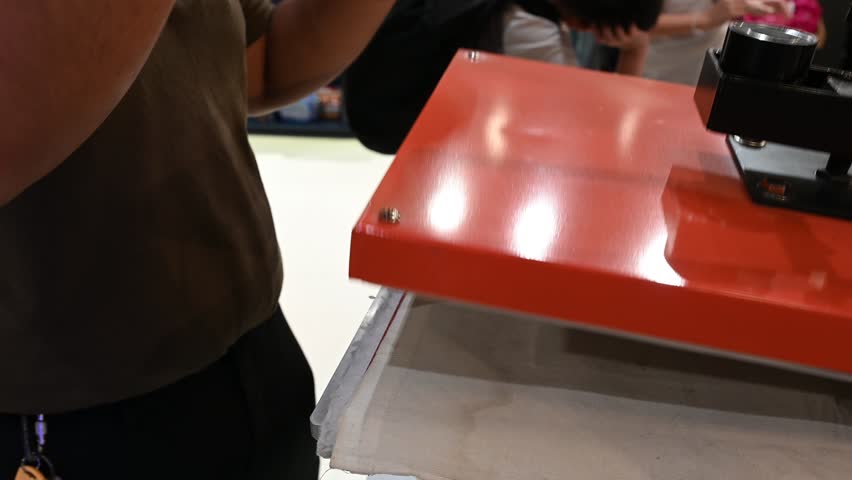 Bangkok, Thailand - 18th December 2025: Man manually printing alphabets on a pouch using an industrial printing machine, showcasing hands-on packaging, craftsmanship, manufacturing process, and small-scale production.