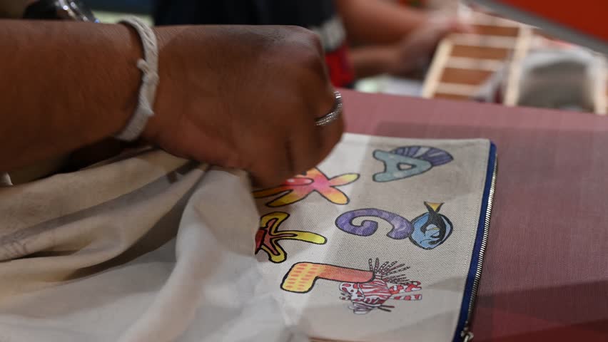 Bangkok, Thailand - 18th December 2025: Man manually printing alphabets on a pouch using an industrial printing machine, showcasing hands-on packaging, craftsmanship, manufacturing process, and small-scale production.