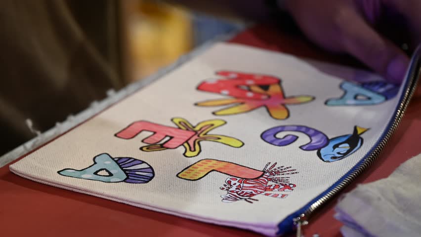 Bangkok, Thailand - 18th December 2025: Man manually printing alphabets on a pouch using an industrial printing machine, showcasing hands-on packaging, craftsmanship, manufacturing process, and small-scale production.