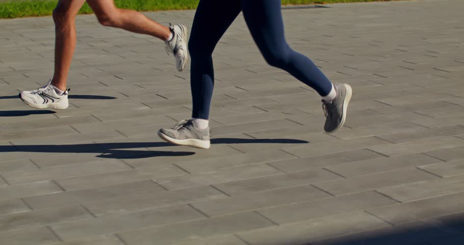 Man and woman running outdoors, close-up of their legs, unrecognizable person