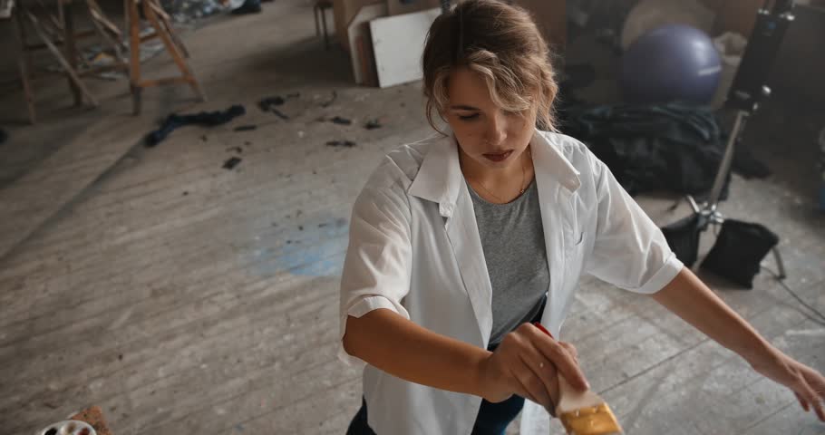 Creative woman painter concentrating on her artwork in a messy studio. High-angle view of a talented artist creating a masterpiece