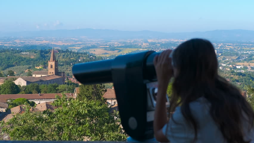 Young woman using binoculars to view perugia, italy. Young traveler looking through coin-operated binoculars at the city of perugia from a scenic viewpoint, enjoying the panoramic italian landscape