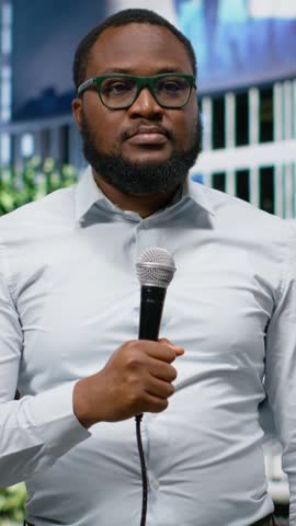 Vertical Video African american reporter on busy city street holding microphone during a live interview, conveying news coverage and public information in modern metropolitan background. Camera B.