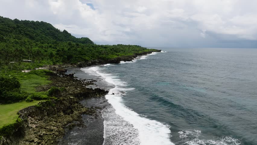 Rocky coastline with tropical forest and ocean waves hitting the shore. Siargao, Philippines.