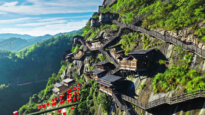 Aerial shot of traditional wooden house built on steep cliffside with mountain landscape and blue sky. The famous Wangxiang Valley Scenic Area is located in Jiangxi, China.