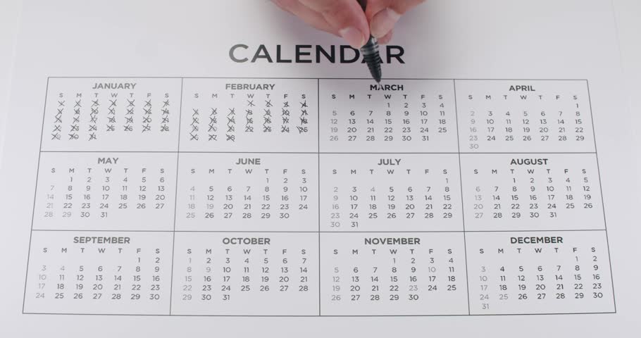 A man's hand marks dates off on a yearly calendar with a black pen. Useful for deadlines, appointments, business, and events. Marking Dates On Calendar