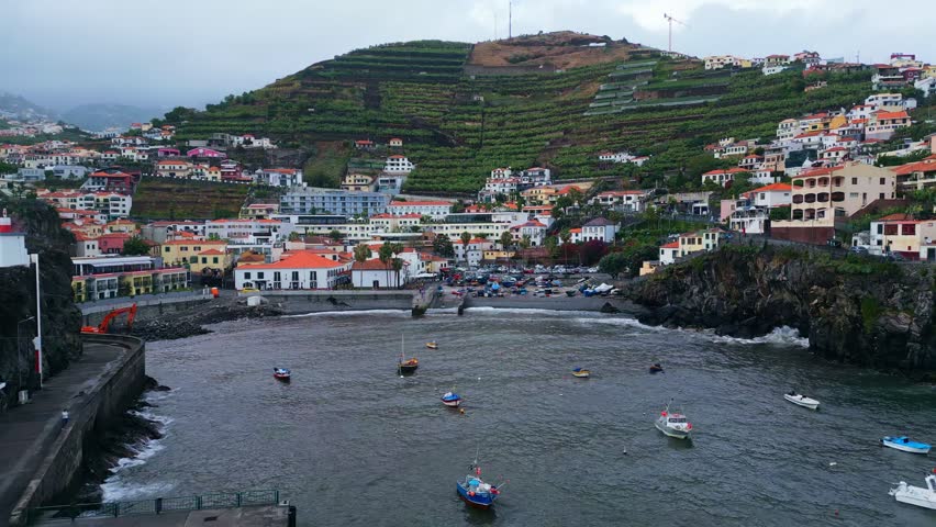 Aerial view of small fishing boats and coastal scenery in Câmara de Lobos, Madeira, Portugal, showing hillside homes, terraced vineyards and a scenic harbour landscape