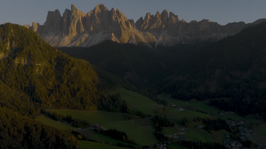 Cinematic aerial view of the Dolomites in Italy, rugged alpine peaks glowing at dawn, dramatic cliffs and deep shadowed valleys creating a serene high-altitude mood