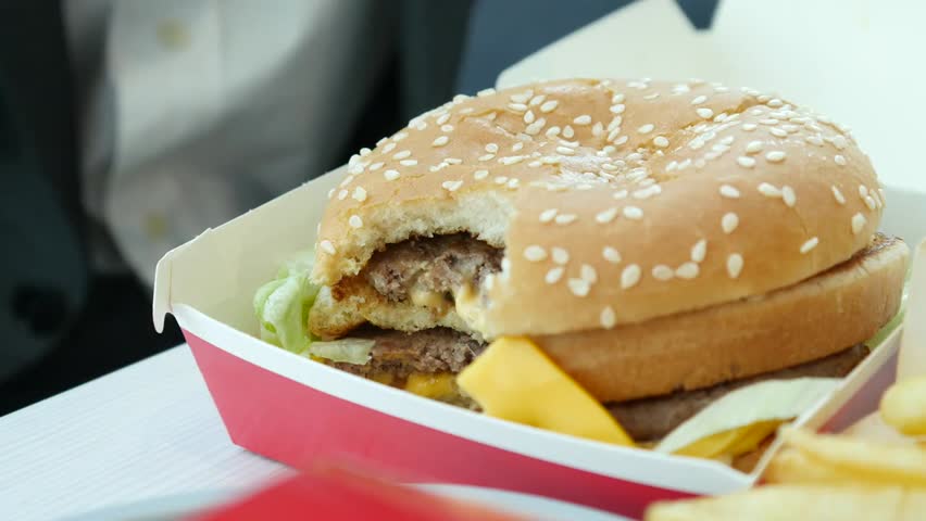 Man enjoying a burger with hands at a fast food restaurant, eating quickly and savoring classic McDonald’s flavors in a casual setting.