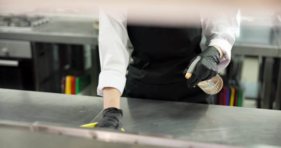 Chef, cleaning and hands with cloth, kitchen and sanitation with chemical or maintenance of surface. Wiping, workstation and person with spray for disinfection, hygiene and food safety in restaurant
