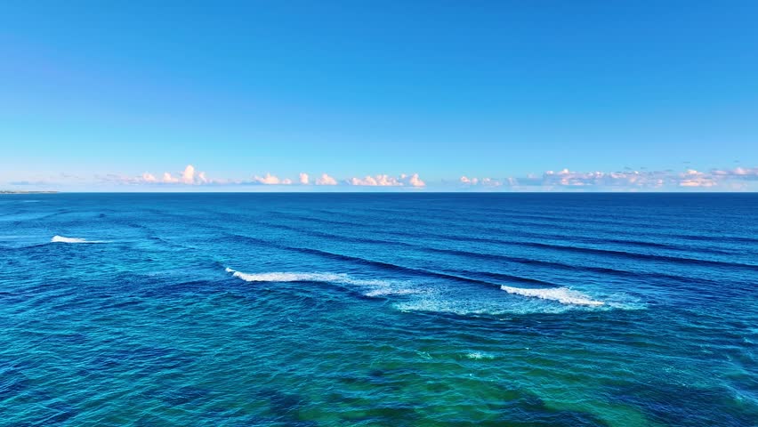 White clouds over the blue ocean in the morning. Drone flight over blue sea waves to a pink horizon. Delicate pink clouds in an azure sky. Sunrise at sea. Open ocean. Cruise. Sea voyage.