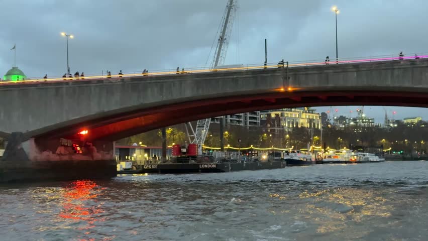 Evening cityscape showing the illuminated london bridge over the river thames with tourist boats and city buildings in the background