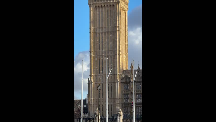 Upward tilting camera movement showing the iconic elizabeth tower, famously known as big ben, against a blue sky with some clouds in london, uk