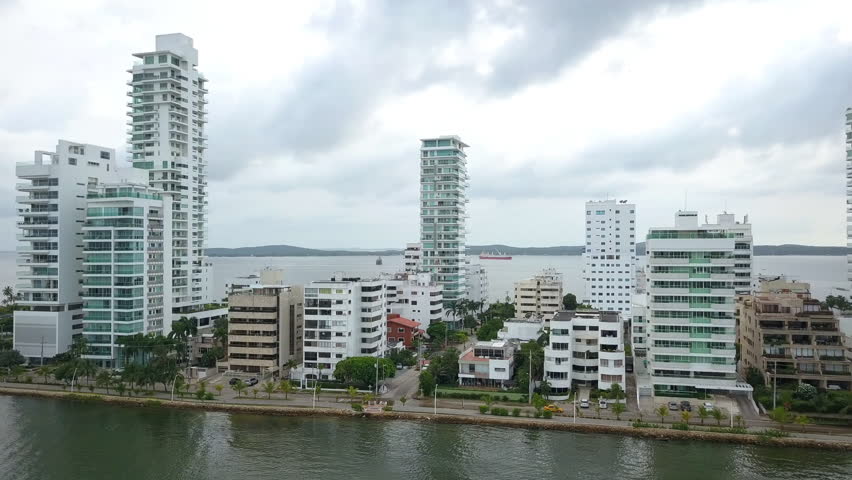 Aerial semi orbit around modern coastal city buildings along waterfront with calm water and overcast daylight.