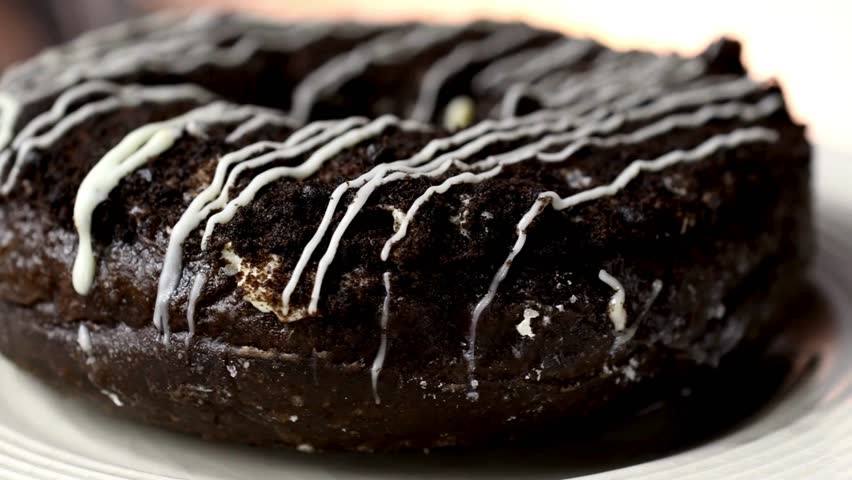 Rich chocolate donut topped with creamy white icing, beautifully presented on a decorative plate. An inviting sweet treat perfect for any dessert lover.
