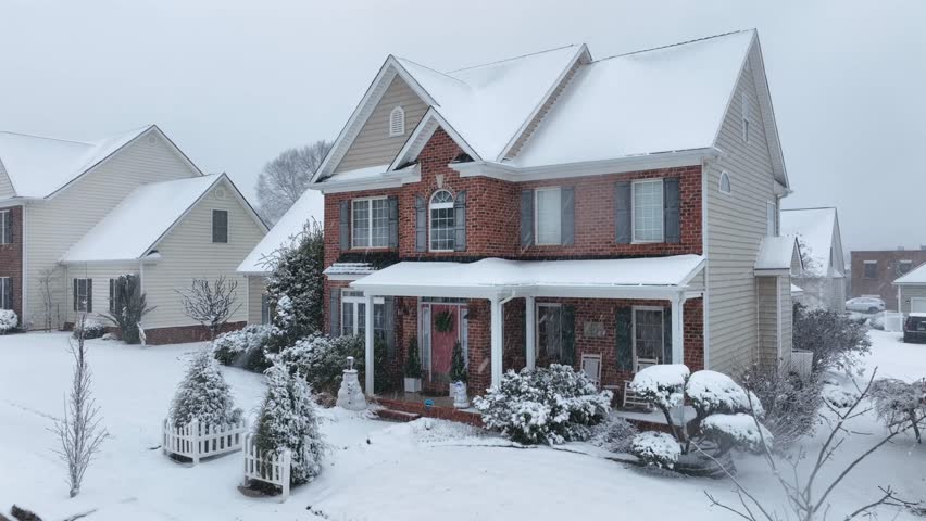 Aerial view of Snow-covered single-family house in an American suburban neighborhood during winter, with classic brick architecture, front porch and fresh snowfall. Snowman on entrance of home in USA.