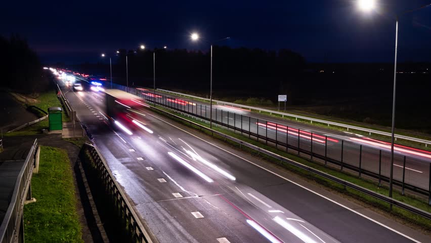 Night highway timelapse showing fast streaking lights across open lanes under bright road lamps