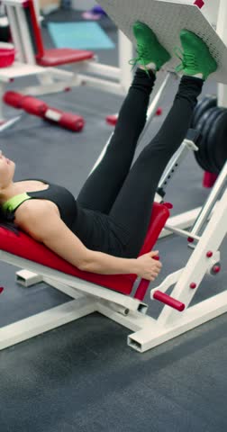 Vertical 4k footage of a middle-aged woman trains her leg muscles with the leg press machine. Using the leg press machine, the woman builds lower body strength through precise and controlled movements