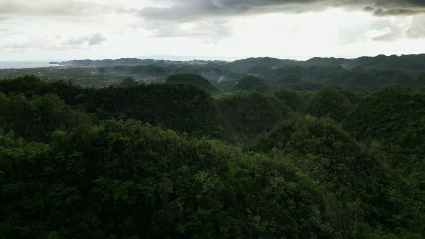 Panoramic aerial forward of dense tropical forest and rolling hills at Buyo, Catanduanes, Philippines during cloudy day.