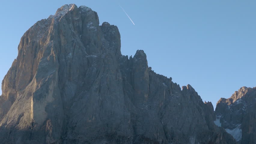 Cinematic aerial view of the Dolomites in Italy, rugged alpine peaks glowing at dawn, dramatic cliffs and deep shadowed valleys creating a serene high-altitude mood