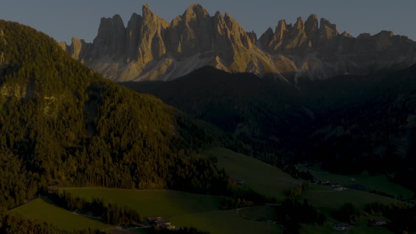 Cinematic aerial view of the Dolomites in Italy, rugged alpine peaks glowing at dawn, dramatic cliffs and deep shadowed valleys creating a serene high-altitude mood