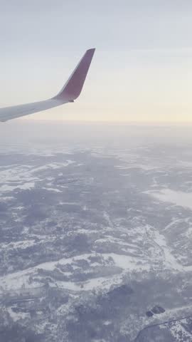 Airplane wing over winter landscape at sunrise from aerial view.