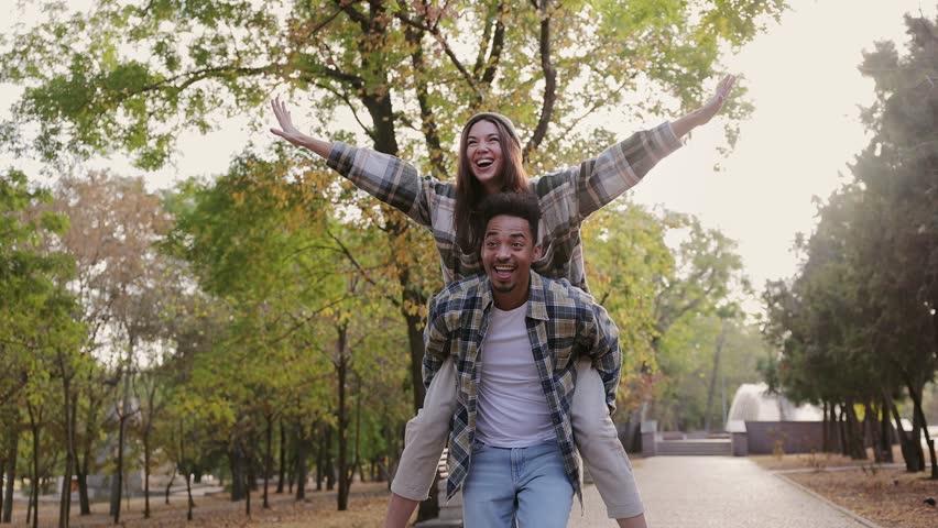 Young couple two friends family man woman wear casual clothes together giving piggyback ride to joyful sit on back walk rest relax in fall city park go down alley outdoors on nature. Urban concept