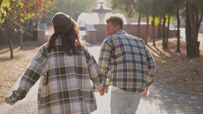 Back view young couple two friends family man woman wearing casual clothes hold hands together run toward fountain walk relax in fall city park go down alley outdoors on nature. Urban leisure concept