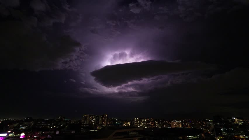 A massive storm cell unleashes its fury over Brisbane, creating a dramatic display of intense lightning illuminating the dark ominous sky and severe thunderstorms sweeping across Southeast Queensland.