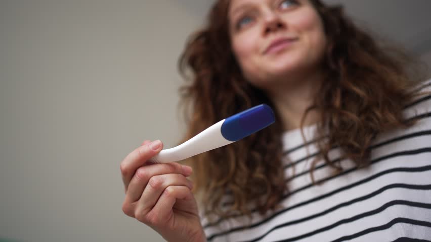 Joyful and emotional woman holding a pregnancy test, smiling and crying with happiness after discovering a positive result, celebrating the long-awaited news of becoming a mother