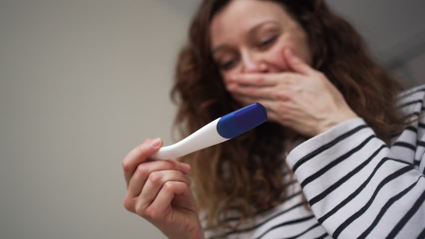 Joyful and emotional woman holding a pregnancy test, smiling and crying with happiness after discovering a positive result, celebrating the long-awaited news of becoming a mother