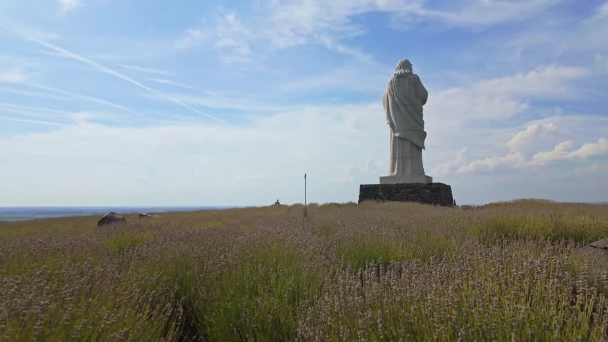 A serene push-in view of the Áldó Krisztus statue in Tarcal, Hungary, surrounded by vibrant lavender fields and a clear autumn sky, showing cultural and spiritual heritage in a peaceful rural setting.