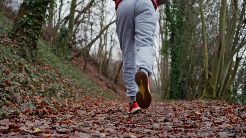Individual Jogging Uphill On Trail Surrounded By Misty Trees Wearing Red Vest, Athlete Moving Briskly Uphill Along Leafcovered Woodland Trail With Misty Surroundings And Red Footwear