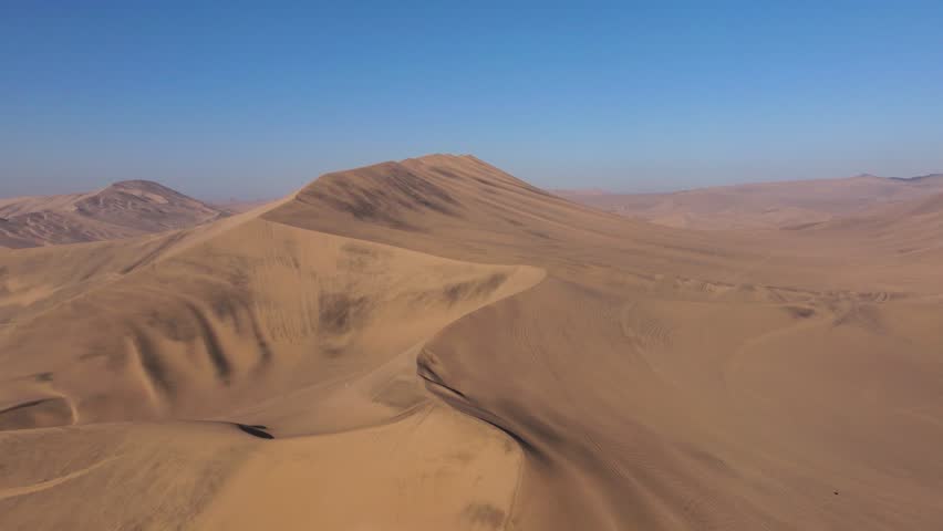 Wind shaped S curve dunes rise and fall in smooth patterns across a quiet Peruvian desert expanse