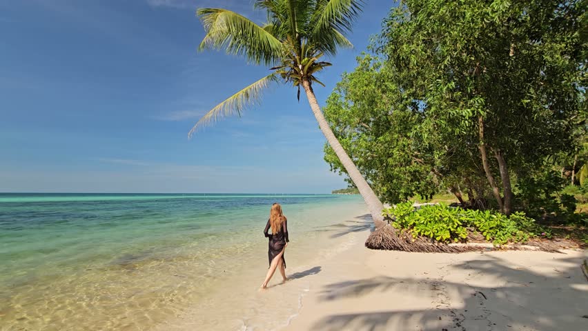 Beautiful young brunette woman in black bikini swimsuit is smiling on tropical sand of Indian sea coastline at summer sunny day