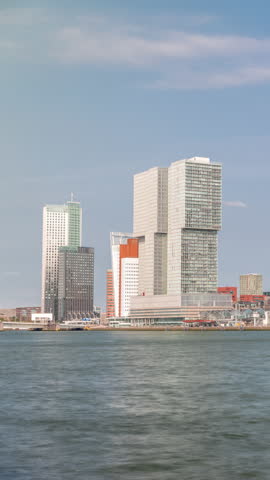 Rotterdam skyline timelapse from Nieuwe Maas River bank to Wilhelminapier and Kop van Zuid. Modern skyscrapers, ship terminal and waterfront in this redeveloped former harbor area with boats passing