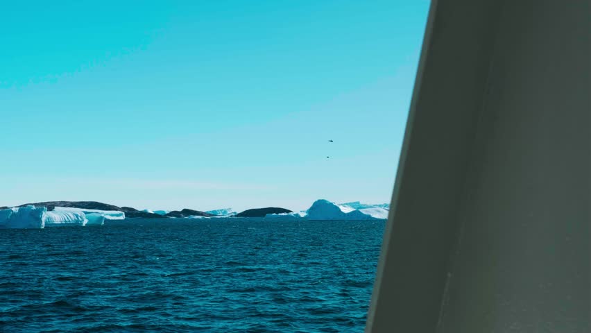 Fly over massive snow covered iceberg drifting blue ocean. Large towering glacier float clear cold water in sunny day. Global warming, climate change. Explore Arctic travel. Winter scene.