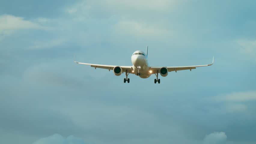 Passenger airplane flying with landing gear extended against blue cloudy sky. Commercial jet approaching runway with wheels down in daylight. Modern aircraft descending through sky with clouds in