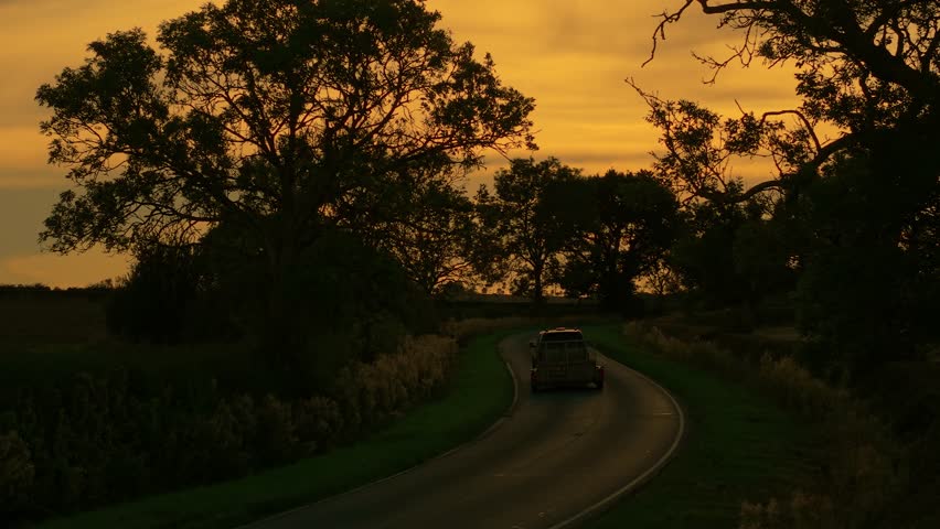 Automobile traveling on countryside road during sunset. Road driving, car traveling highway, countryside nature vacation. Vehicle moving along rural roadway at sundown
