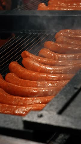 Close-up of sausages sizzling on a barbecue grill at a festive Christmas market with flames and smoke.