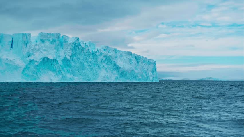 Zoom out panorama giant glacier ice wall iceberg towering on Antarctic coastline polar ocean. Sunny day blue sky, snow covered mountains. Ecology, global warming and climate change. Aerial drone shot