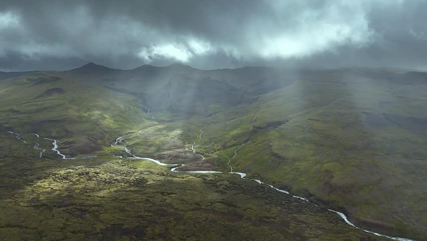 Experience the raw power of nature with this dramatic landscape of a winding river flowing through a valley surrounded by rugged hills and mountains under a stormy sky. The aerial view captures the serene and peaceful atmosphere, inviting you to explore the wild and untouched beauty of the great outdoors.