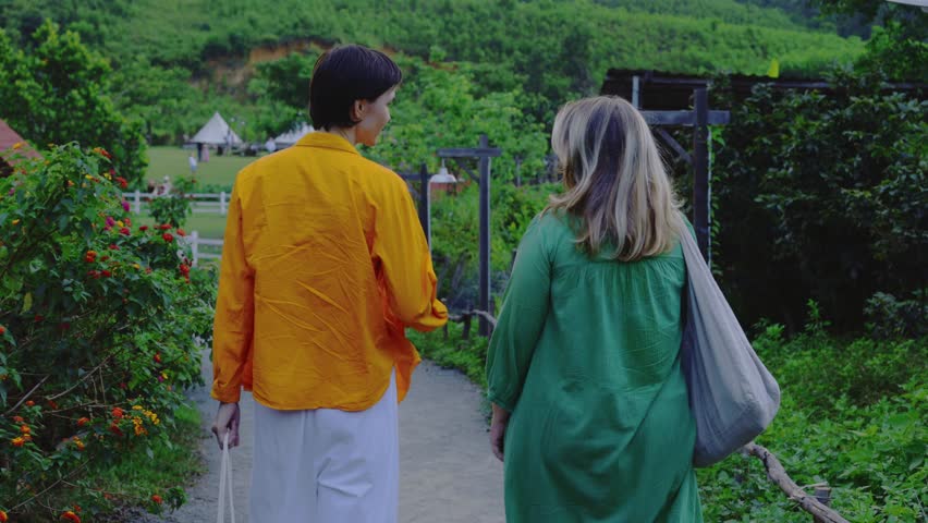 Couple strolling through vibrant garden pathway toward rustic cottages on sunny day