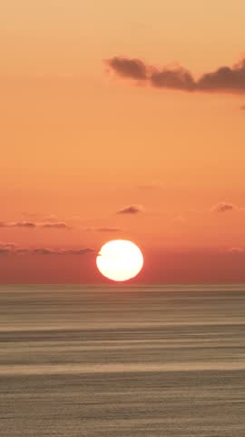 Luminous sun setting over a tranquil sea, painting the sky with warm orange and yellow hues. A serene, beautiful evening seascape. Vertical footage