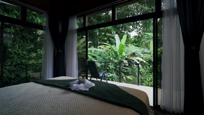 Beautiful hotel bedroom interior with a large bed, folded towels, and a balcony facing a lush tropical jungle. Ideal for vacations
