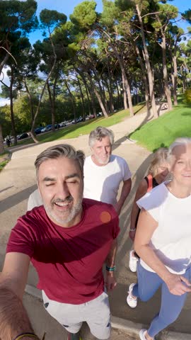 Happy group of mature friends enjoying a healthy lifestyle, jogging together in a sunny park while filming a fun point of view video