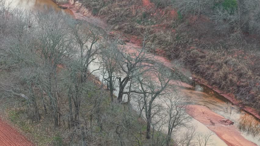 Aerial view of a narrow creek winding through wooded terrain, with exposed sandbars and leafless trees lining the waterway in a quiet rural landscape.