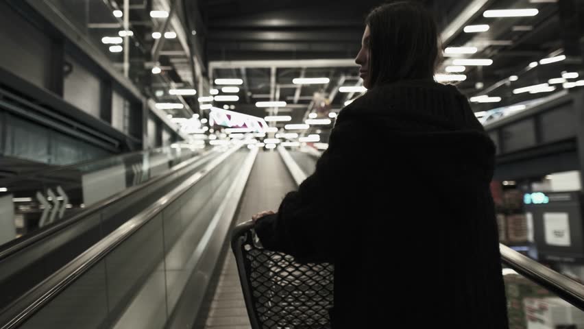 Woman going up escalator with shopping cart in large home improvement store, DIY lifestyle